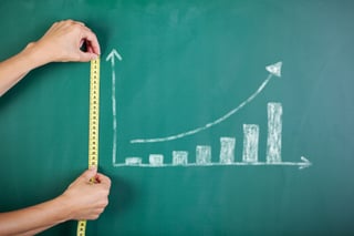 Closeup of womans hands measuring bar graph with tape on blackboard