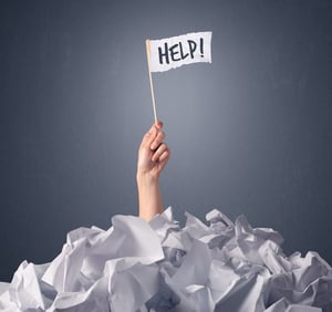 Female hand emerging from crumpled paper pile holding a white flag with help written on it